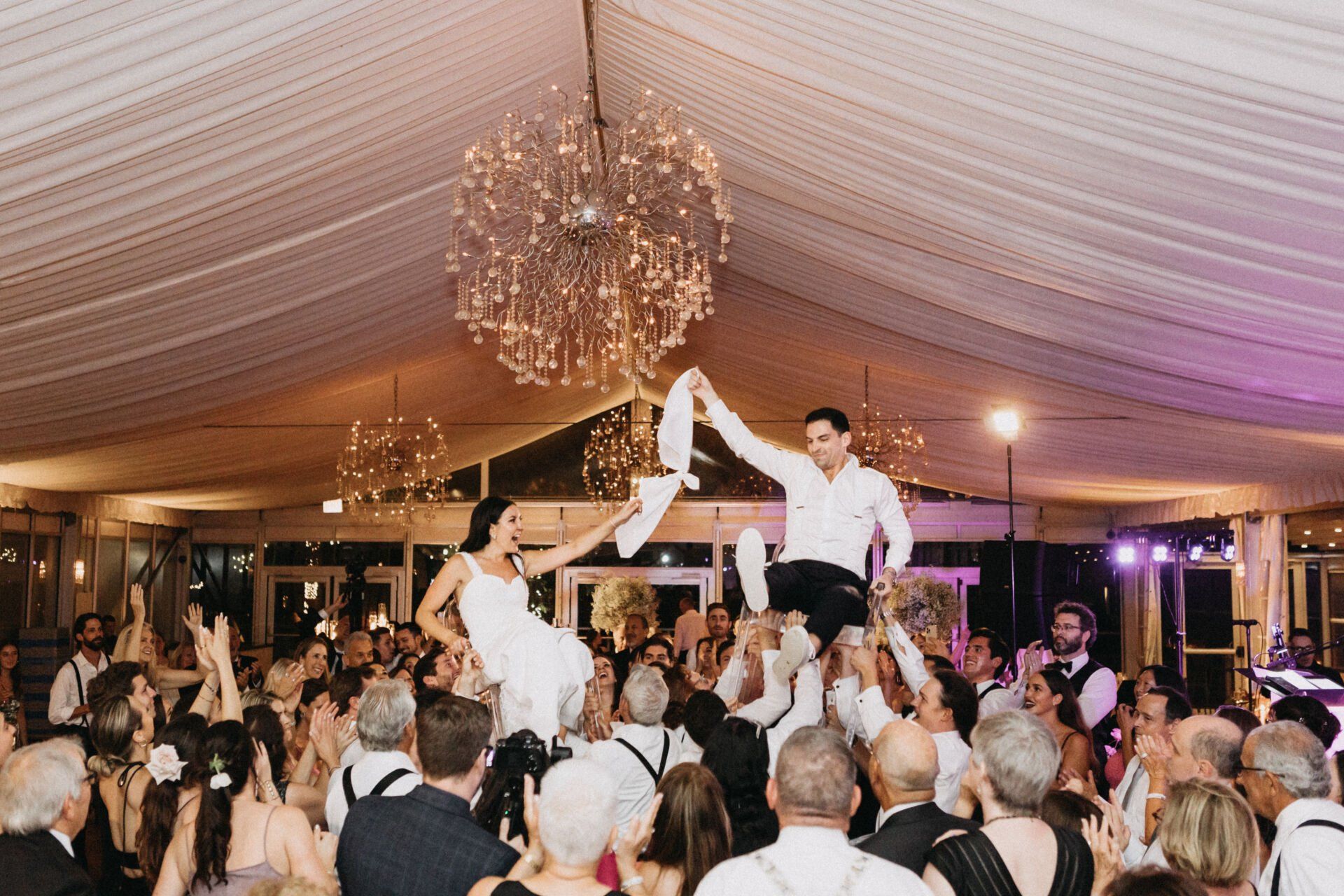 A bride and groom are being lifted on a man 's shoulders at a wedding reception.