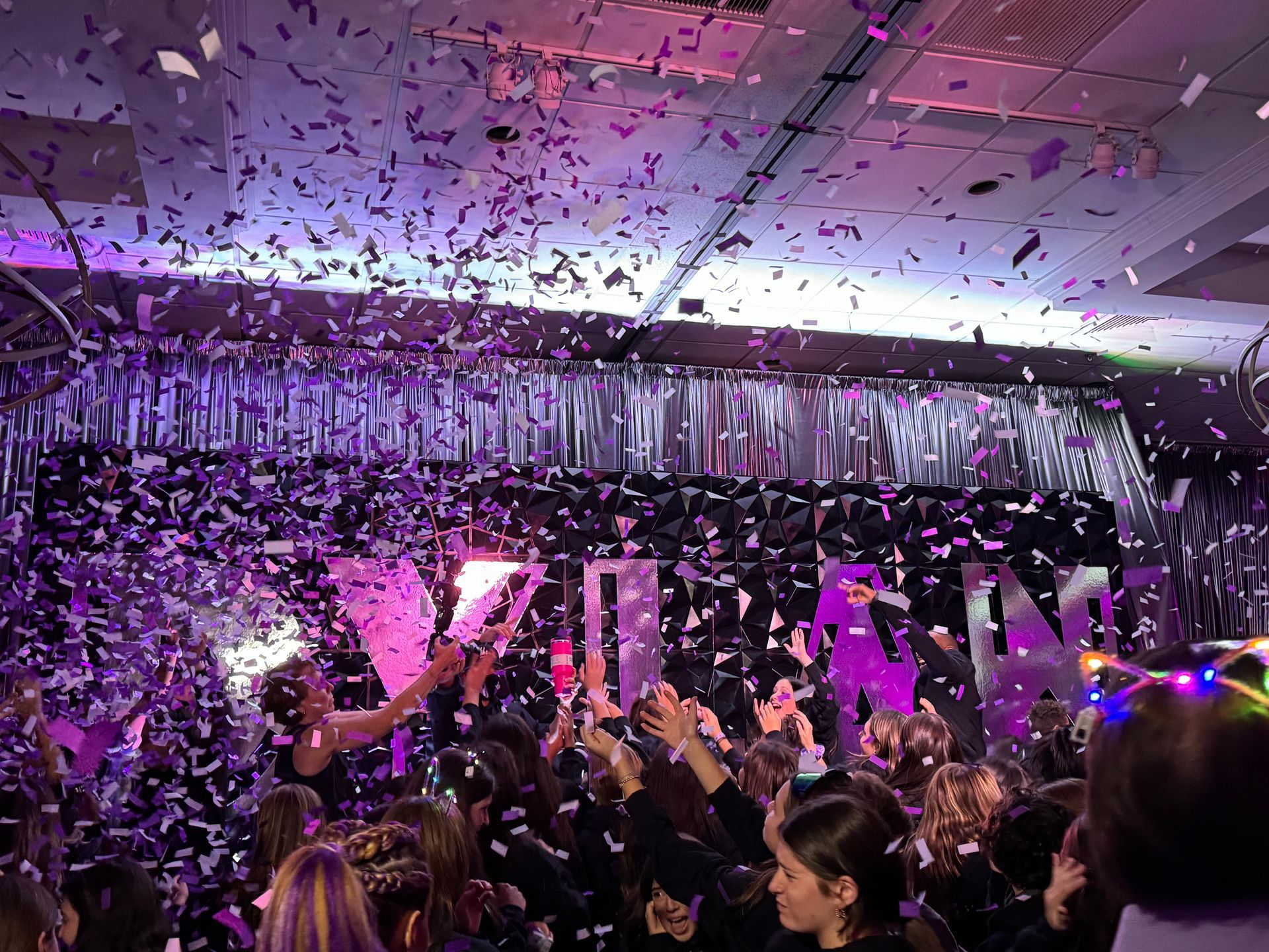 A crowd of people are standing in a room with confetti falling from the ceiling.