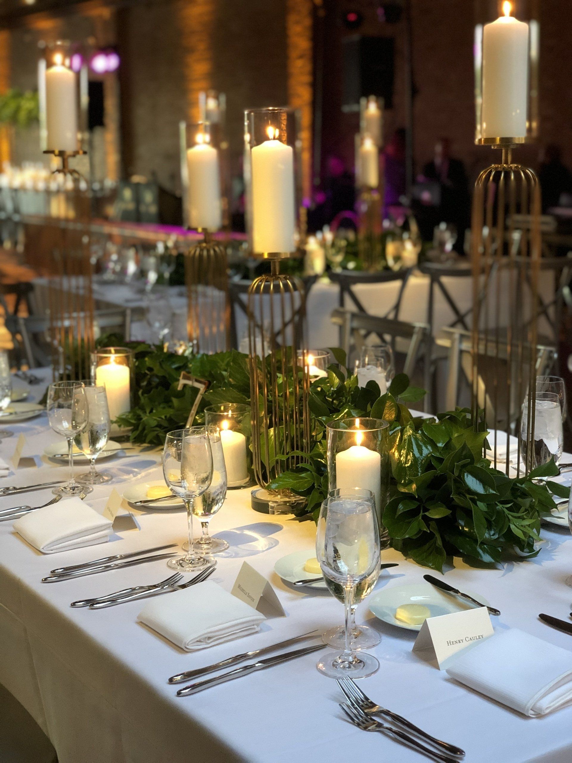 A table set for a wedding reception with candles and greenery.