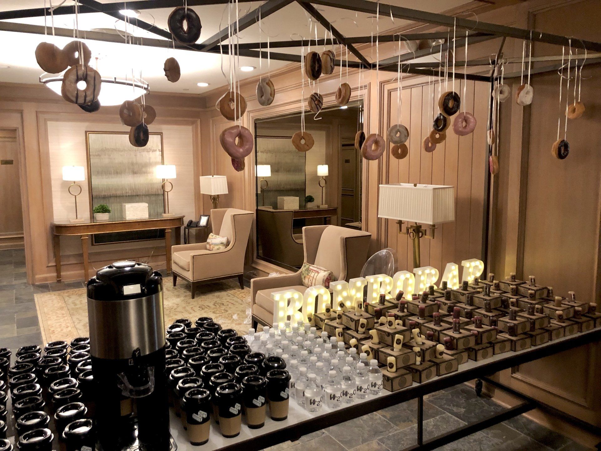 A room with a table full of coffee cups and donuts hanging from the ceiling.