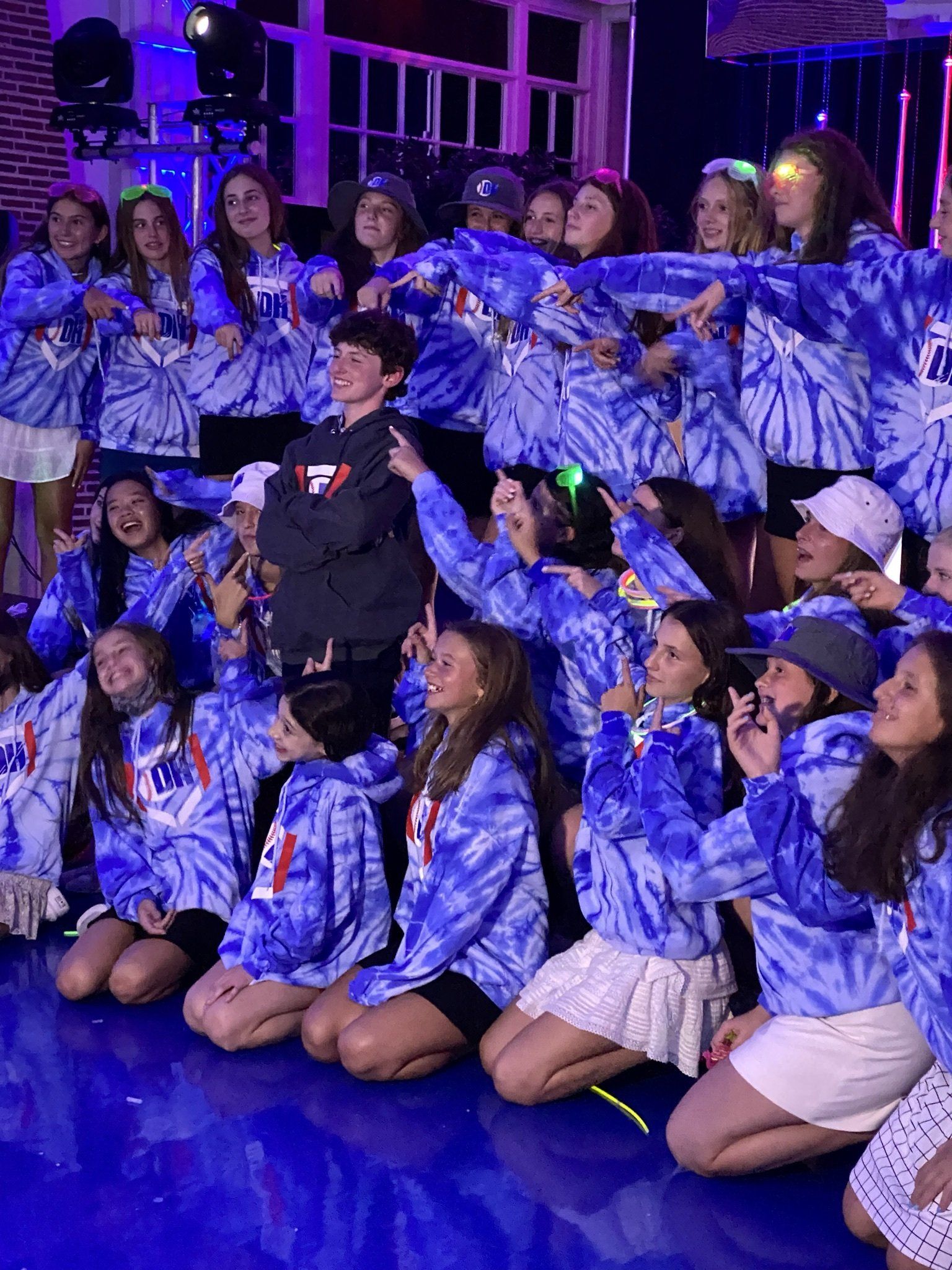 A group of young people wearing blue tie dye shirts are posing for a picture.