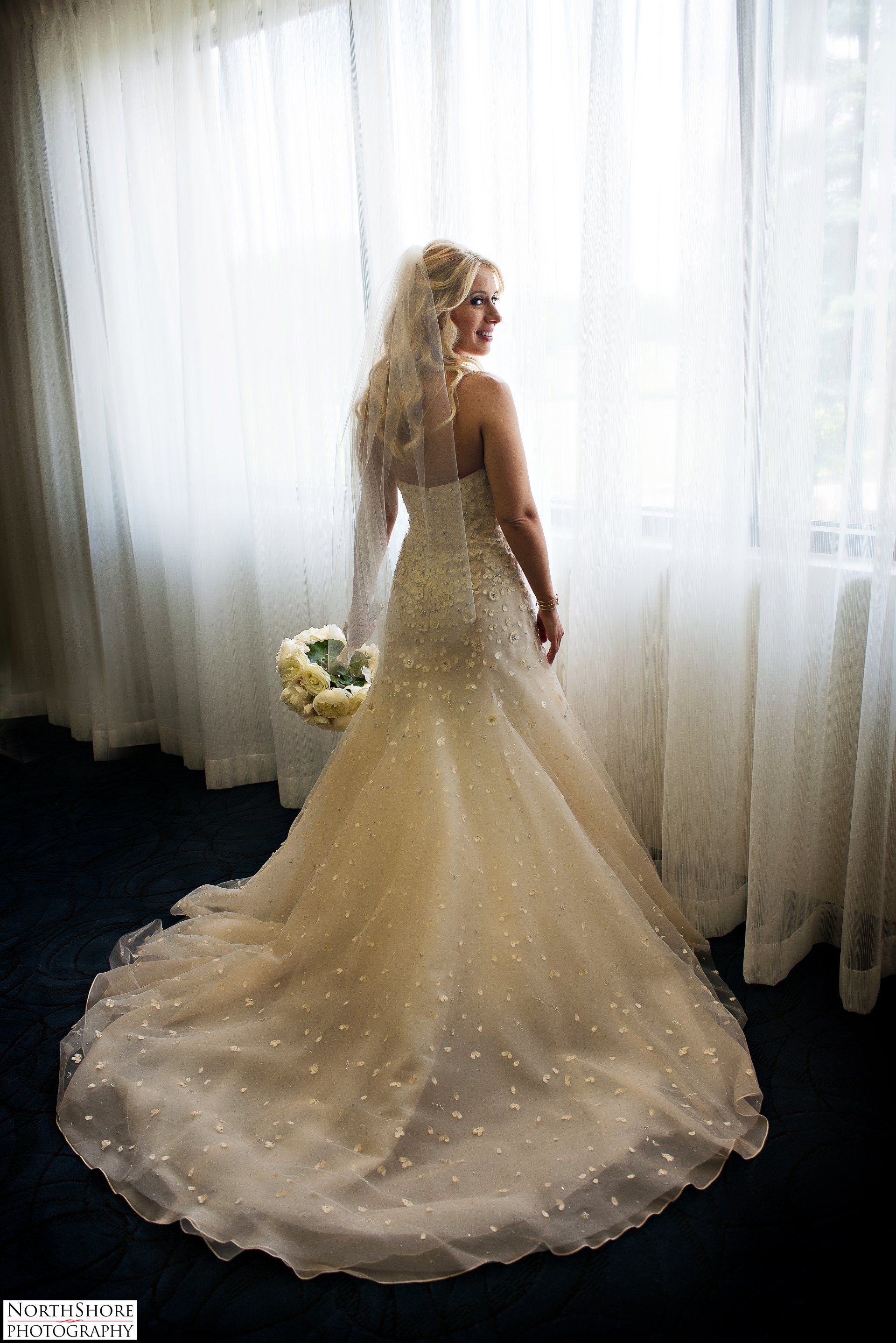 A bride in a wedding dress is standing in front of a window holding a bouquet of flowers.