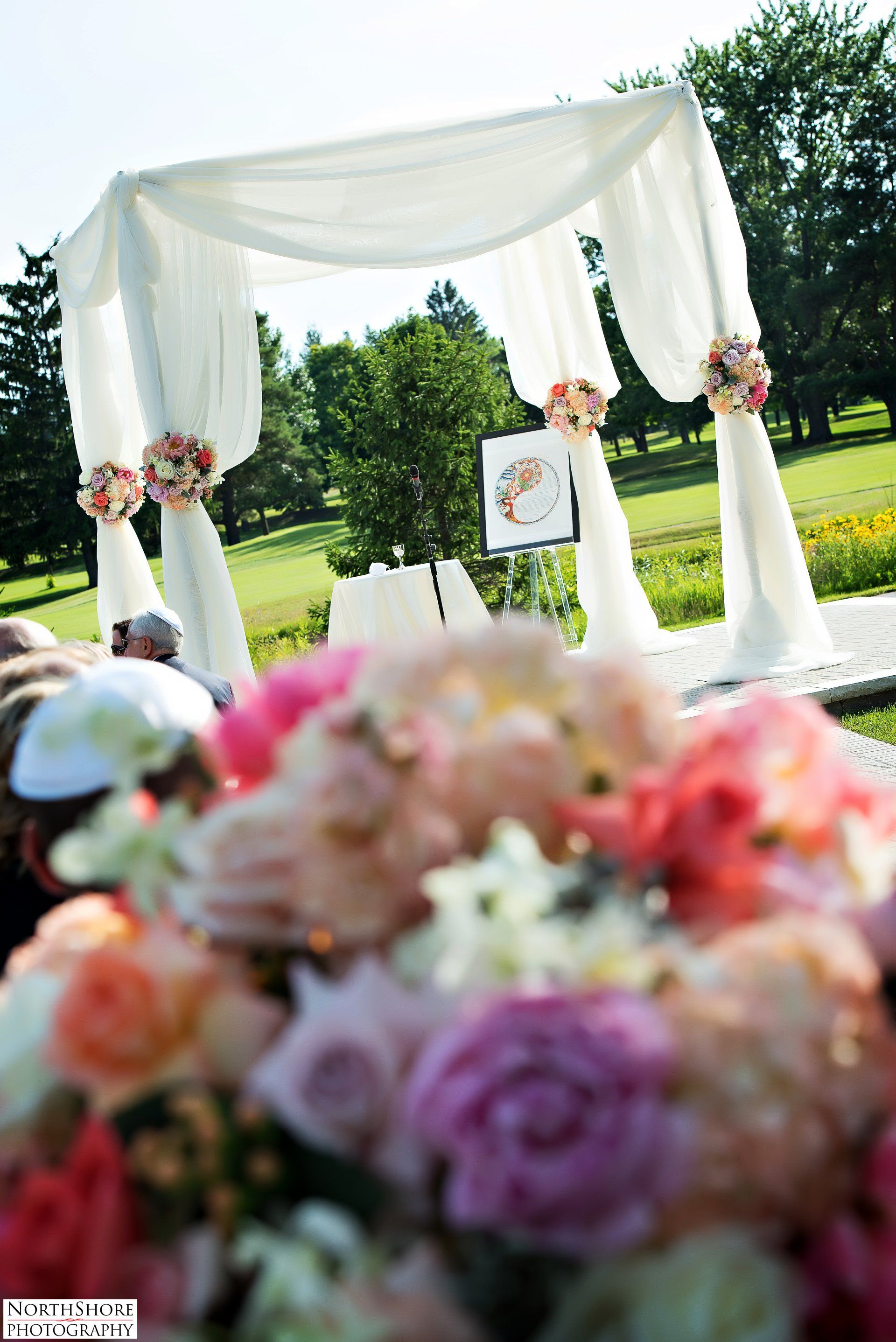 A wedding ceremony is taking place in a park with flowers in the foreground