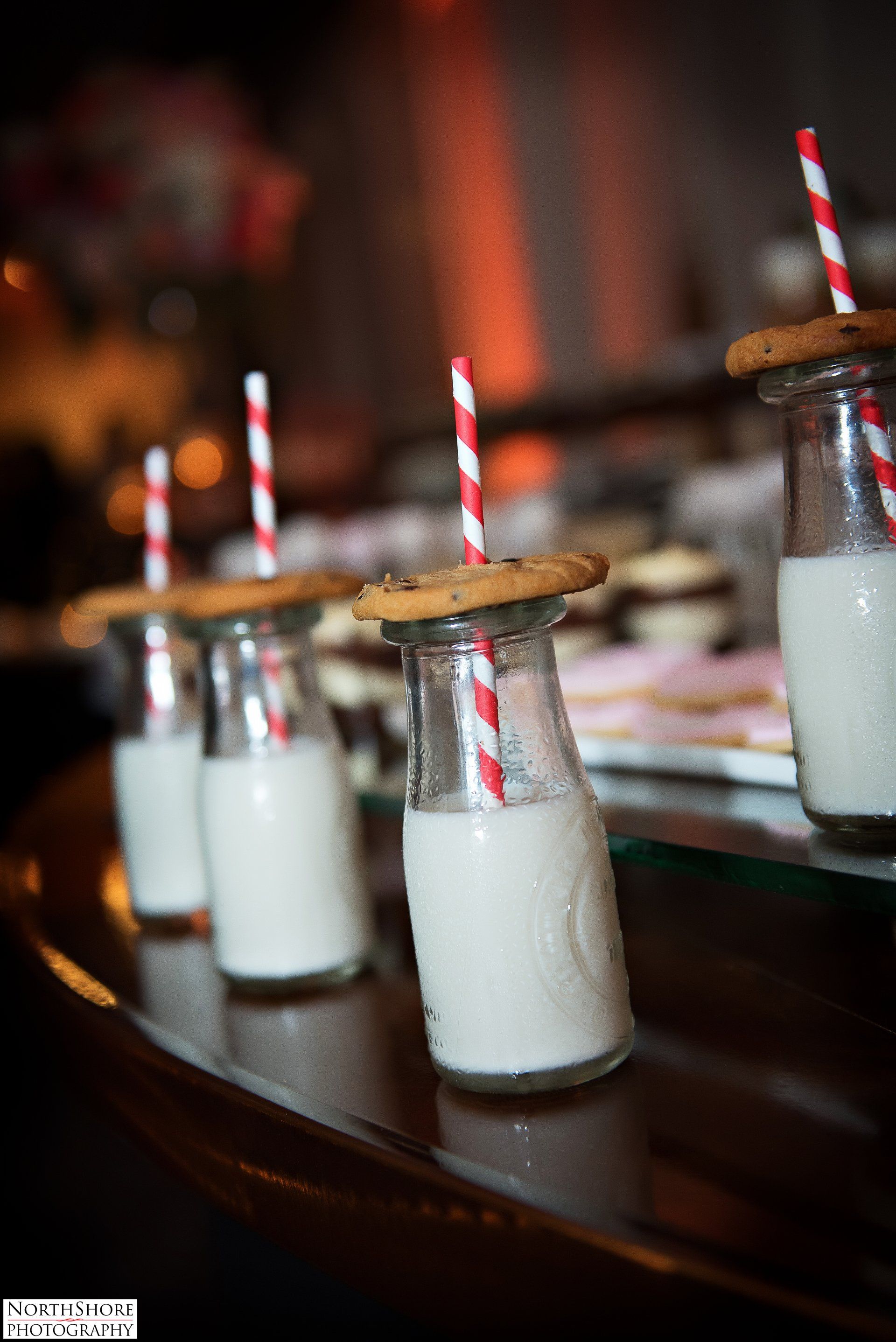 A row of milk bottles with cookies on top and straws.