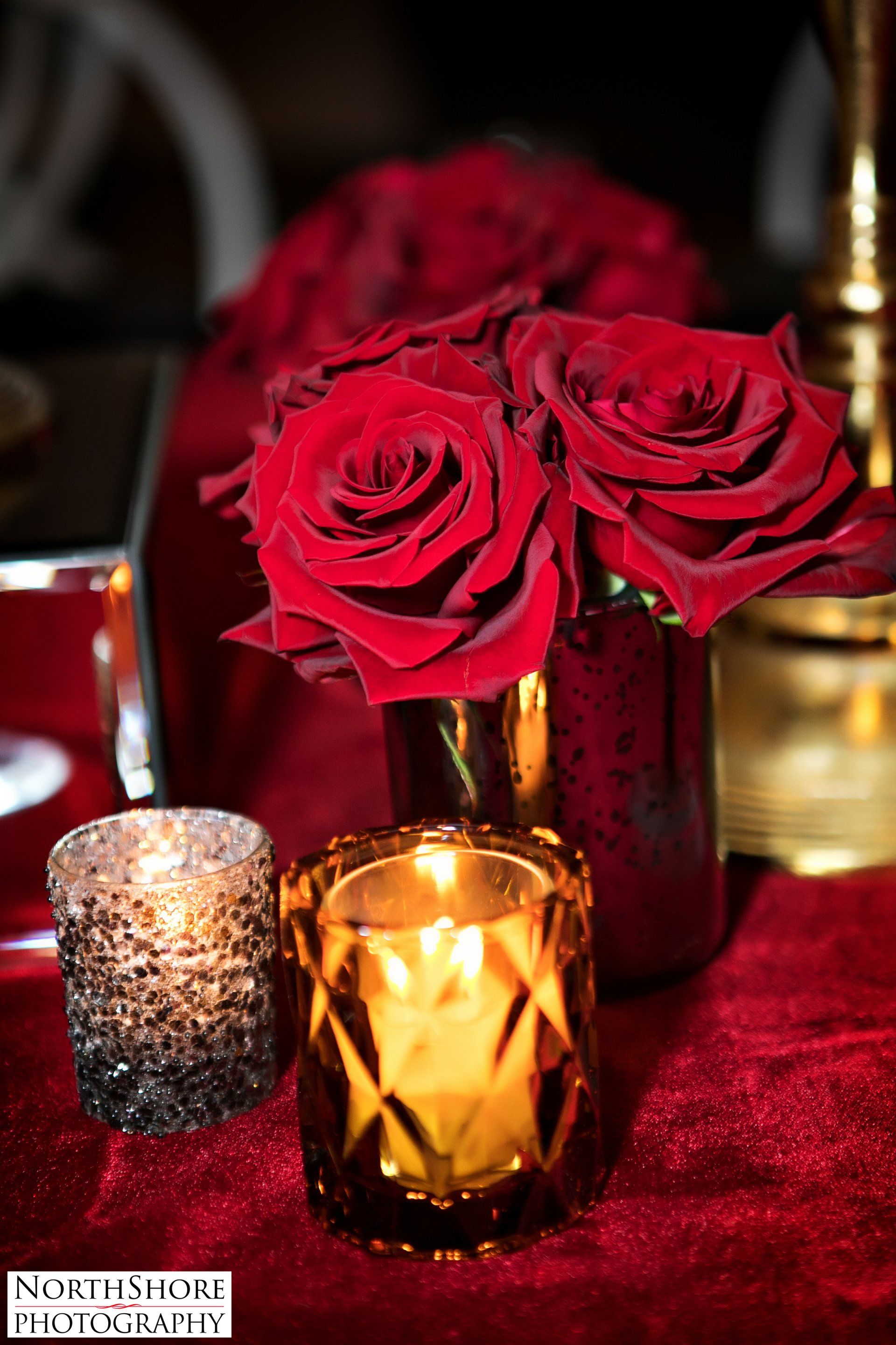 A vase filled with red roses and a candle on a table.