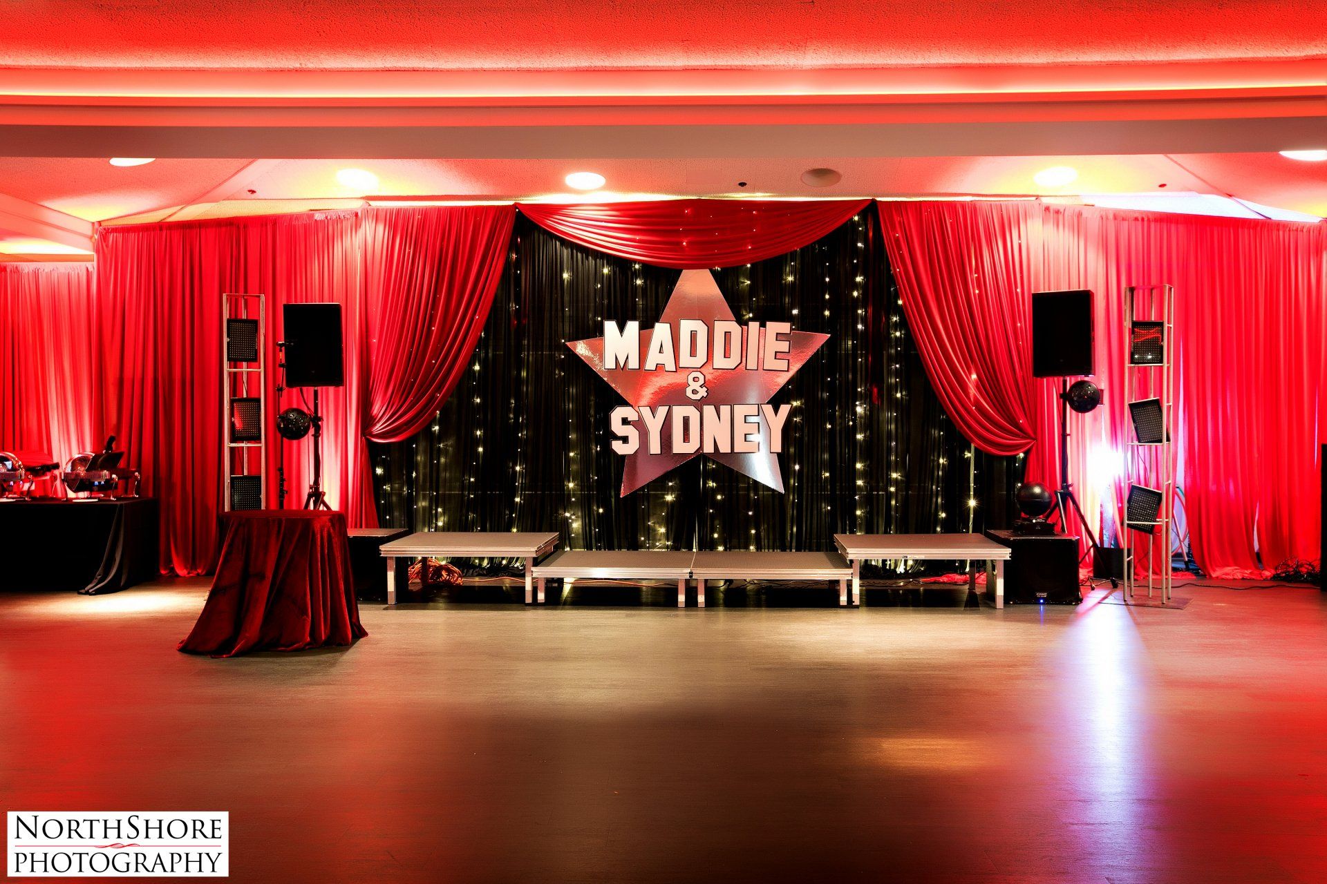 A stage with red curtains and a sign that says maddie and sydney