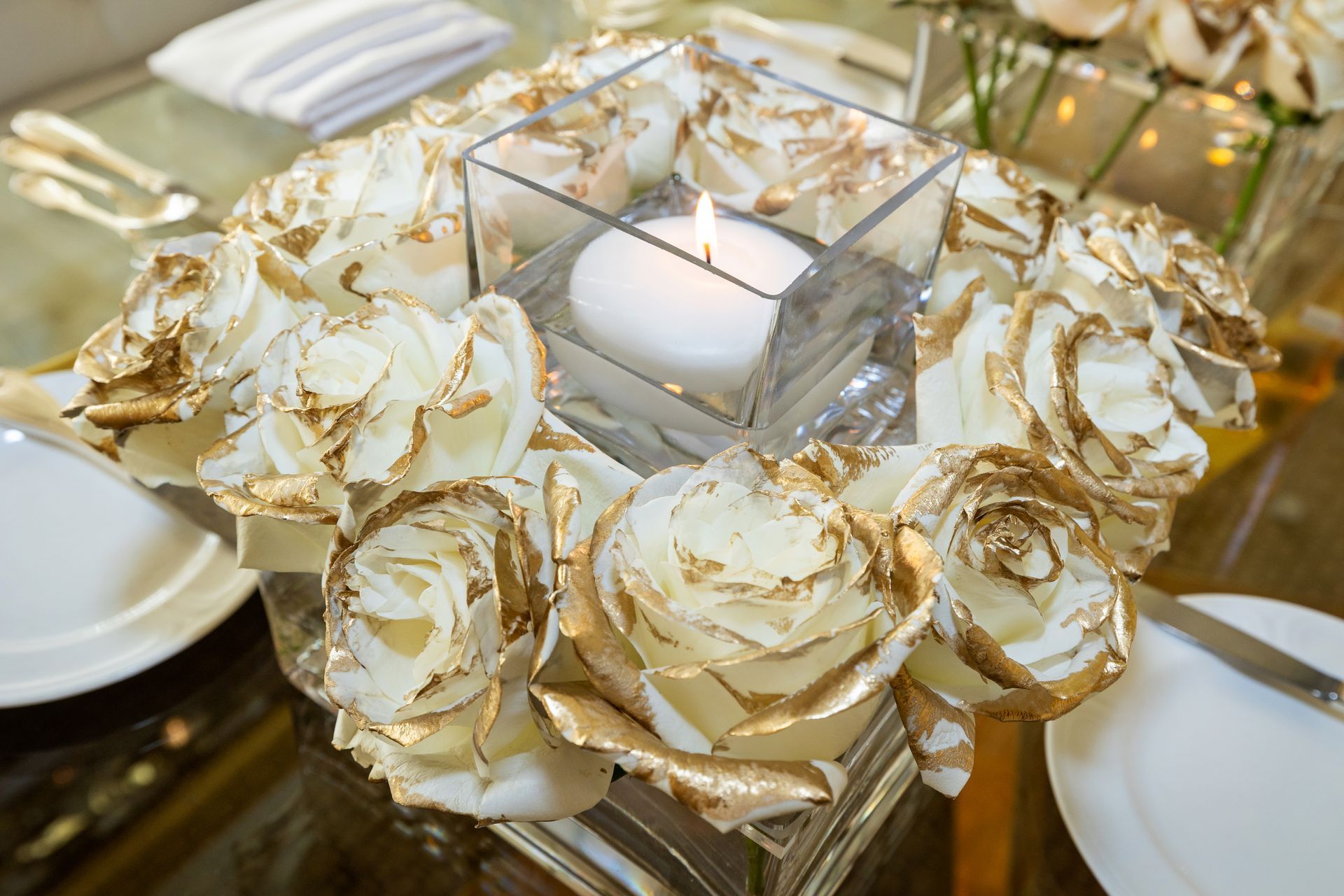 A glass vase filled with gold roses and a candle on a table.