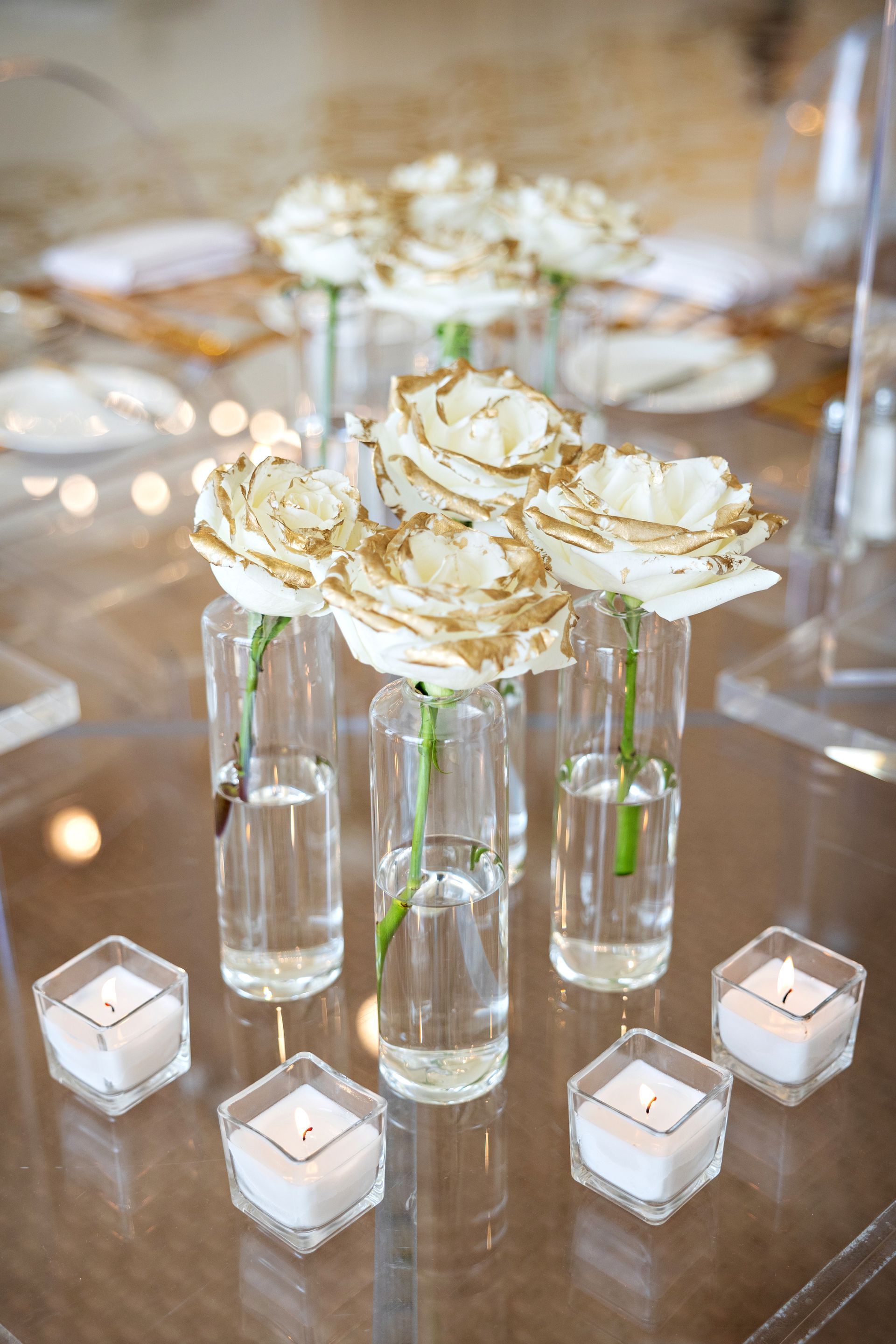 A table topped with vases filled with water and flowers and candles.