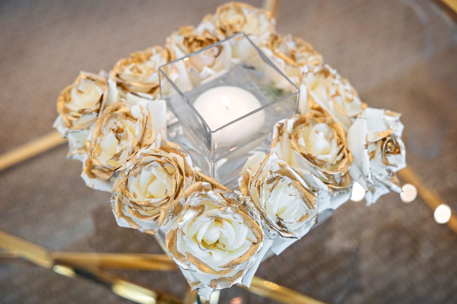 A candle in a glass surrounded by gold roses on a table.