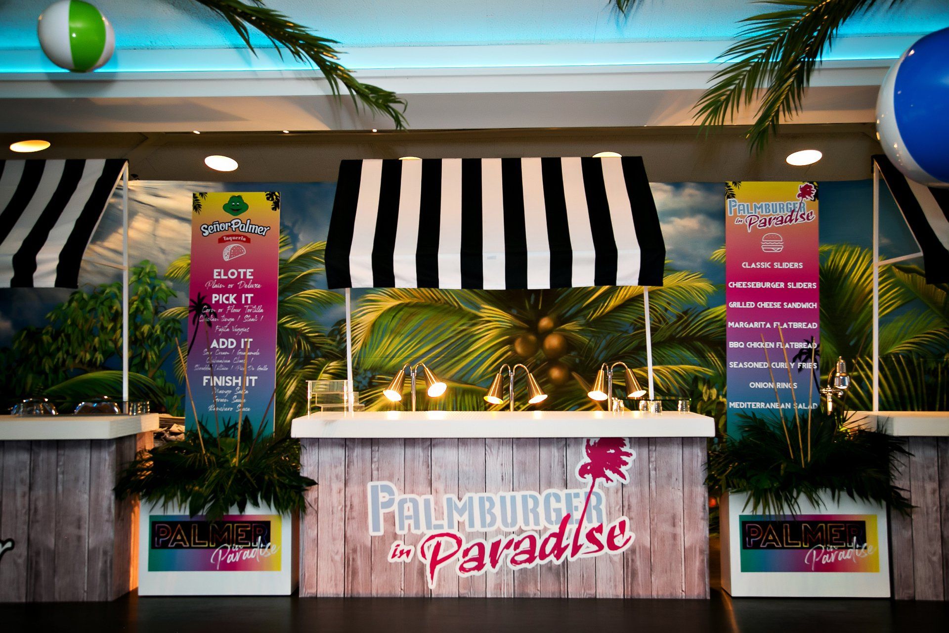 A buffet table with a black and white striped awning and palm trees in the background.