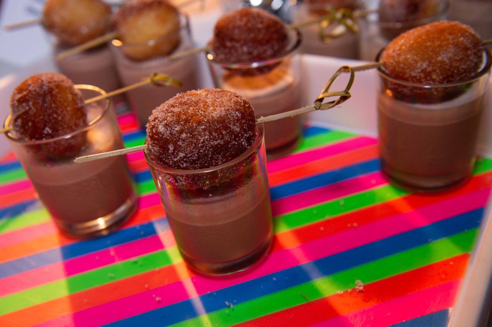 A table topped with glasses filled with chocolate mousse and donuts on sticks.