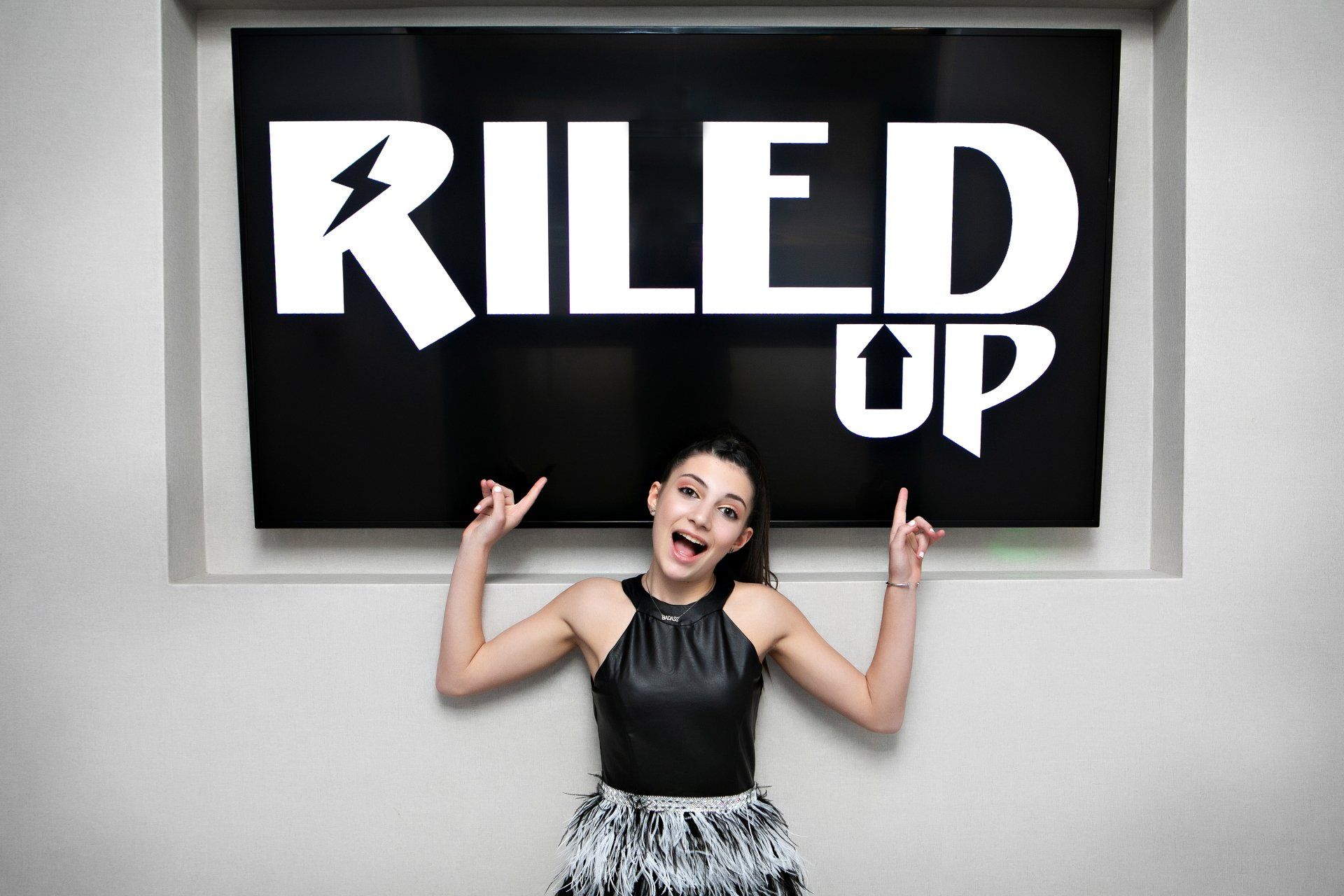A girl is standing in front of a sign that says riled up