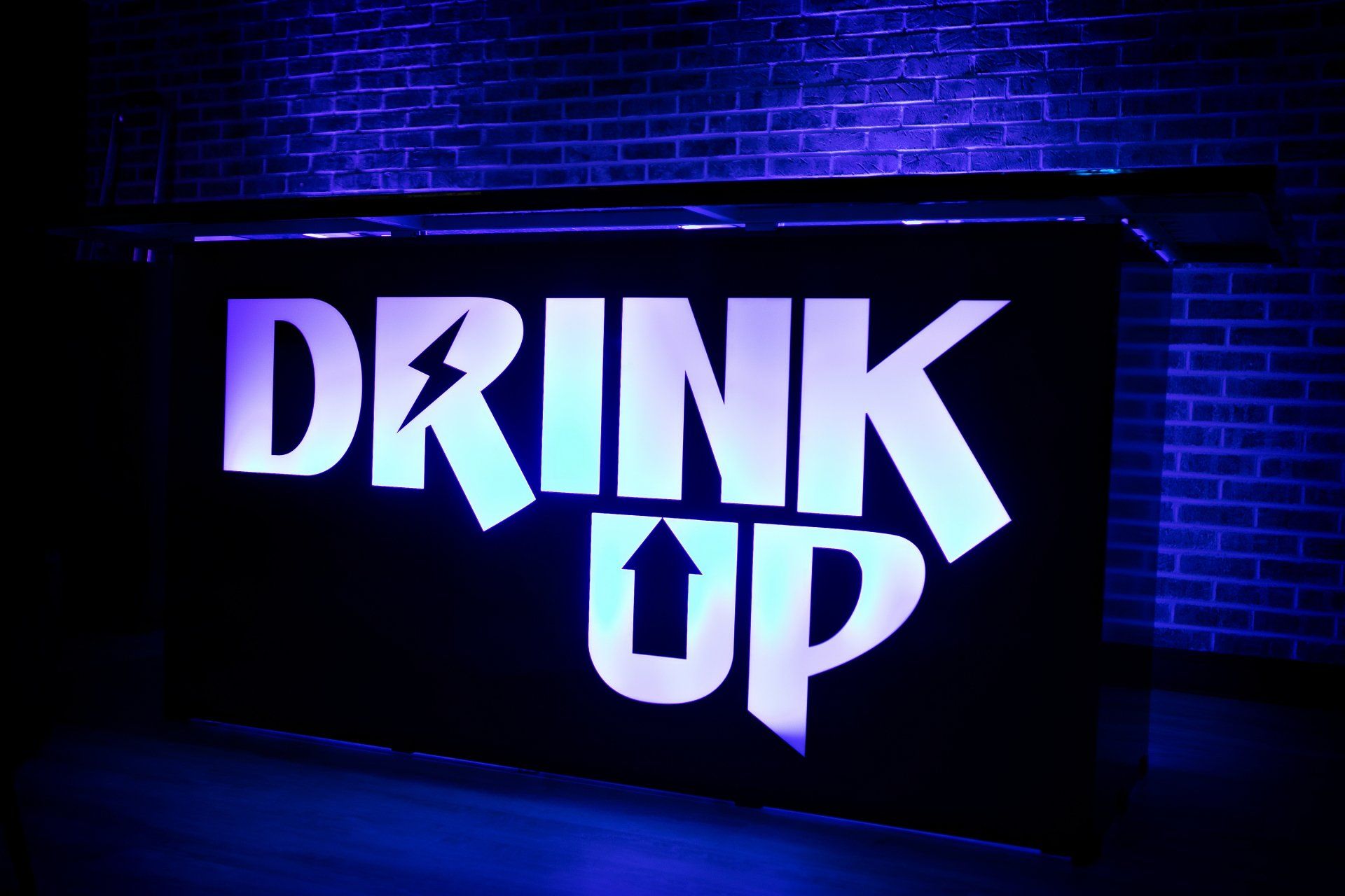 A sign that says drink up in front of a brick wall