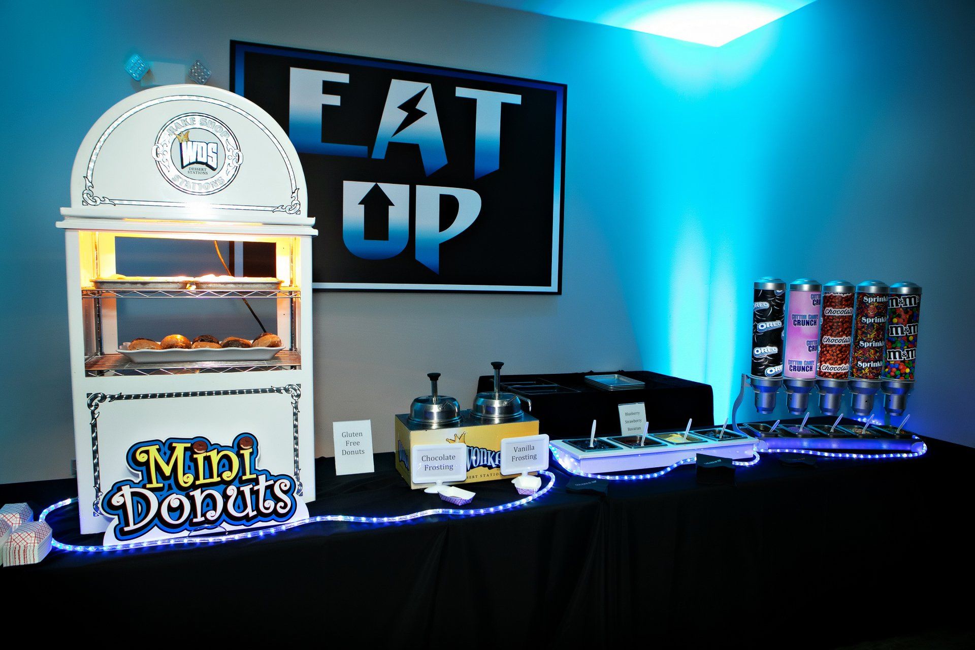 A sign that says eat up is above a display of mini donuts