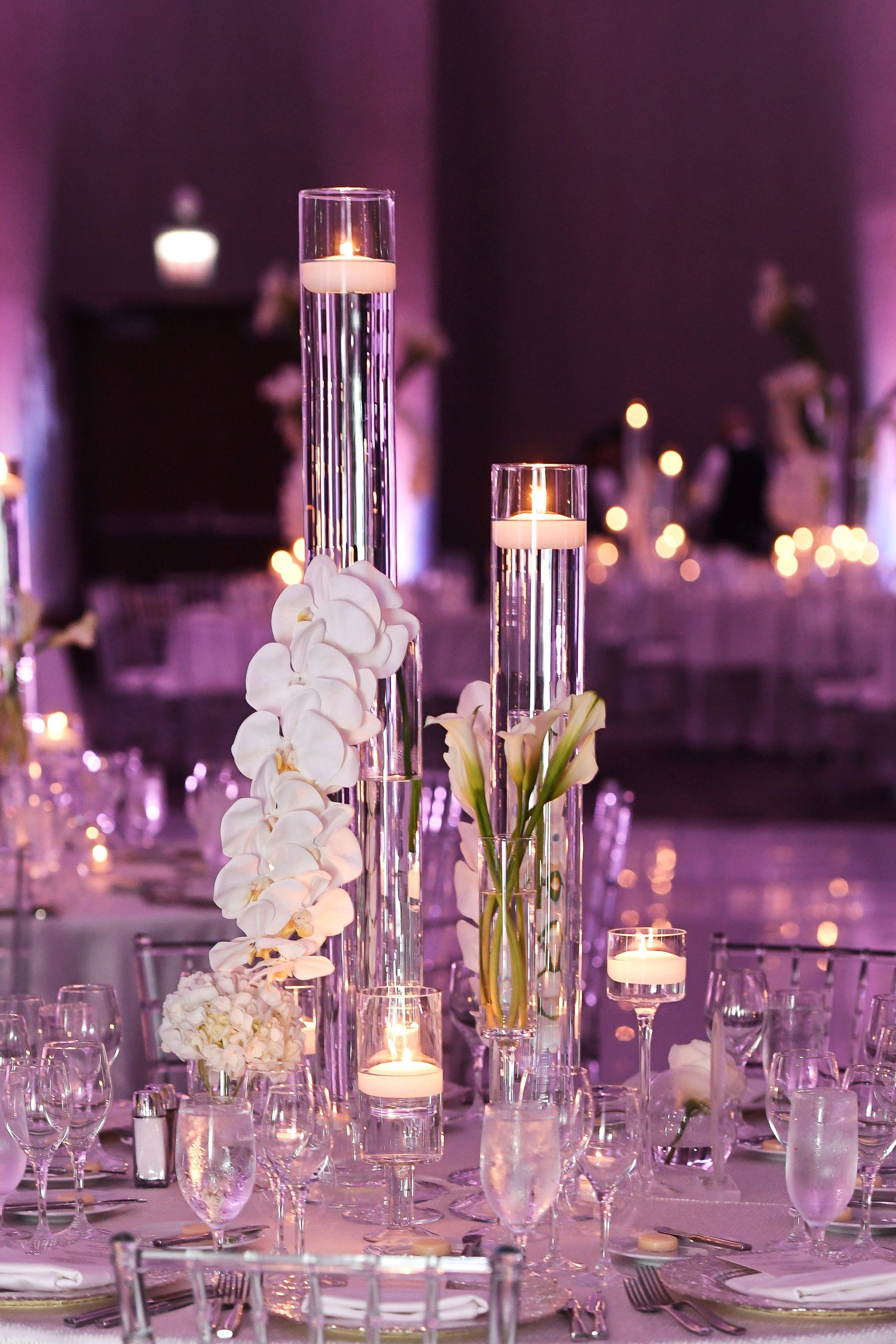 A table set for a wedding reception with candles and flowers in tall vases.
