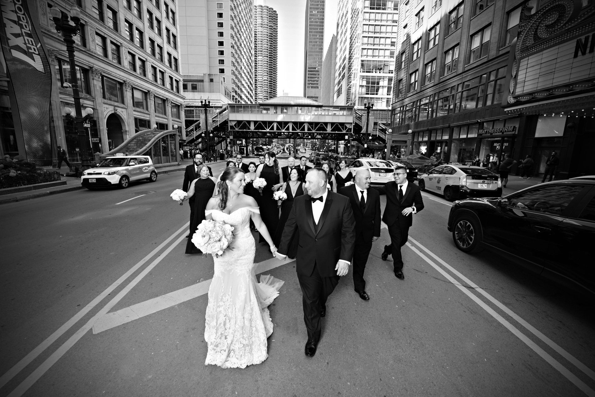 A black and white photo of a bride and groom walking down a city street.