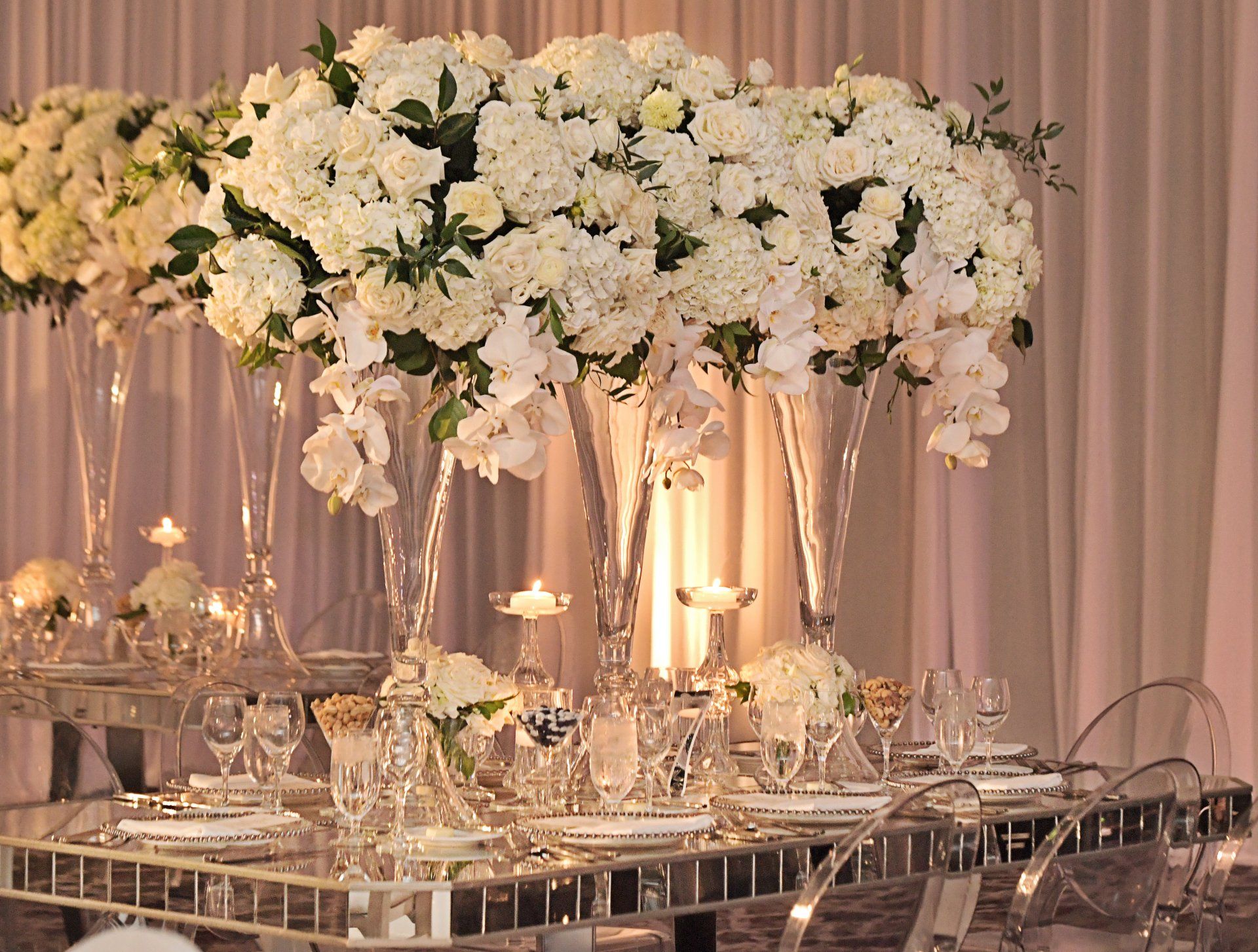 A table set for a wedding reception with white flowers in tall vases.