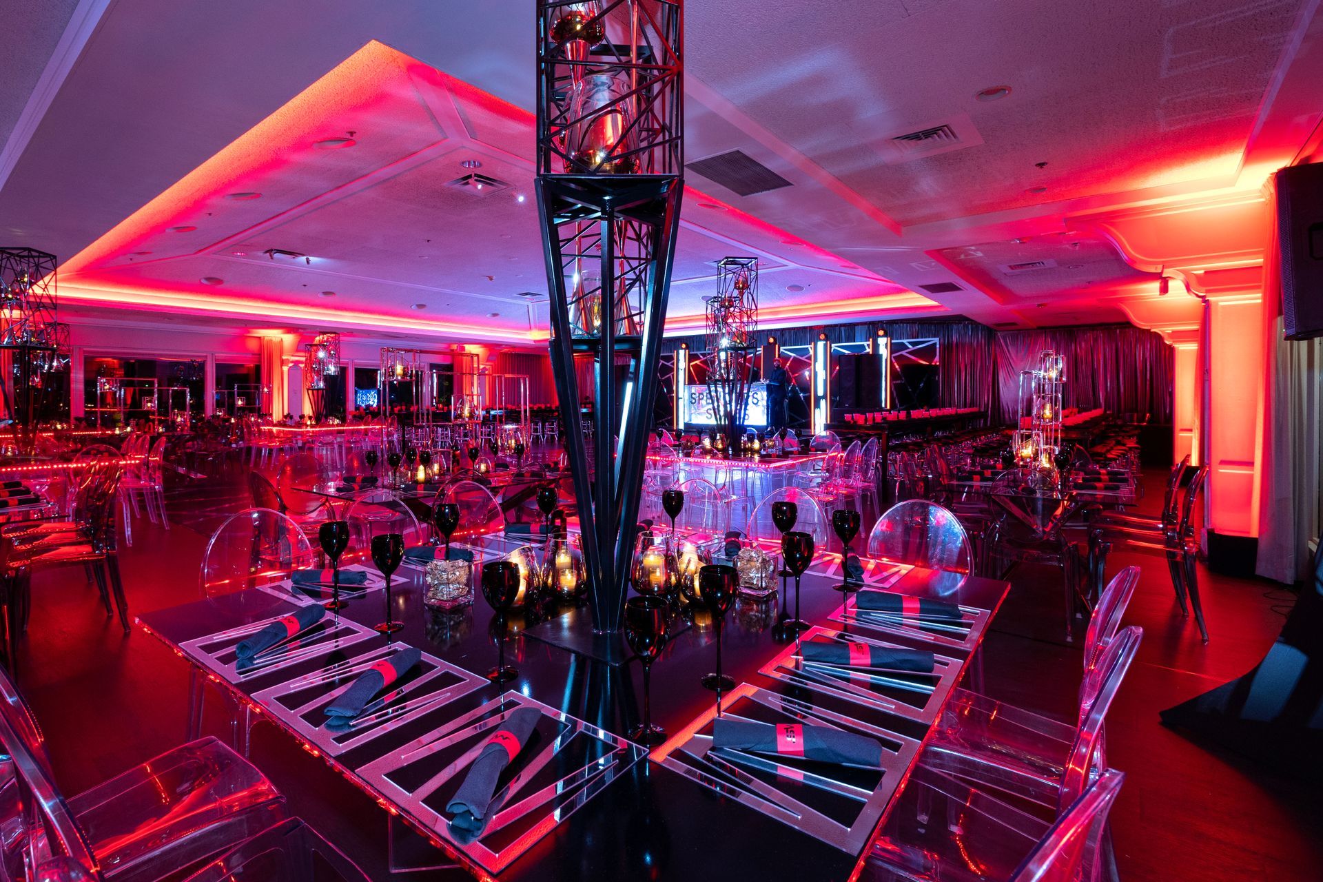 A large room with tables and chairs set up for a party with red lights.