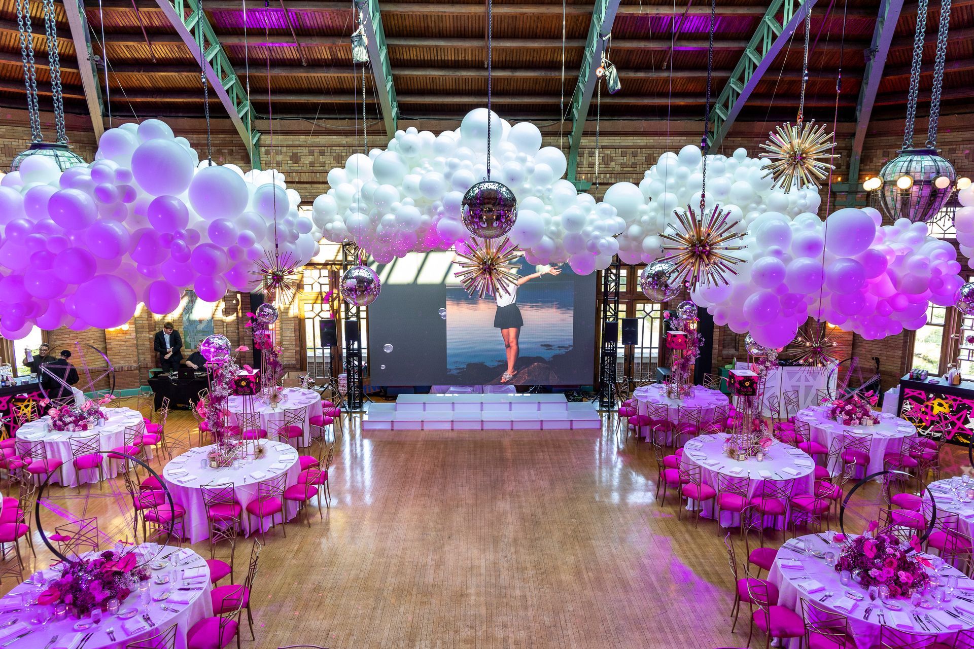 A large room with tables and chairs and balloons hanging from the ceiling.