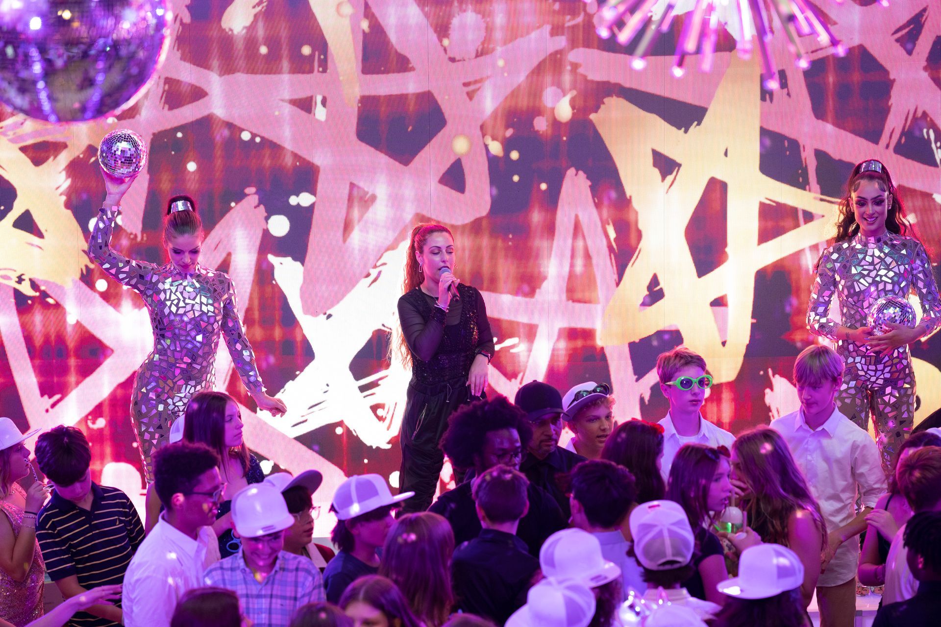 A woman is singing into a microphone in front of a crowd of people at a party.