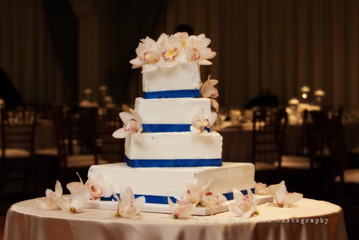 A white and blue wedding cake with flowers on top is on a table.