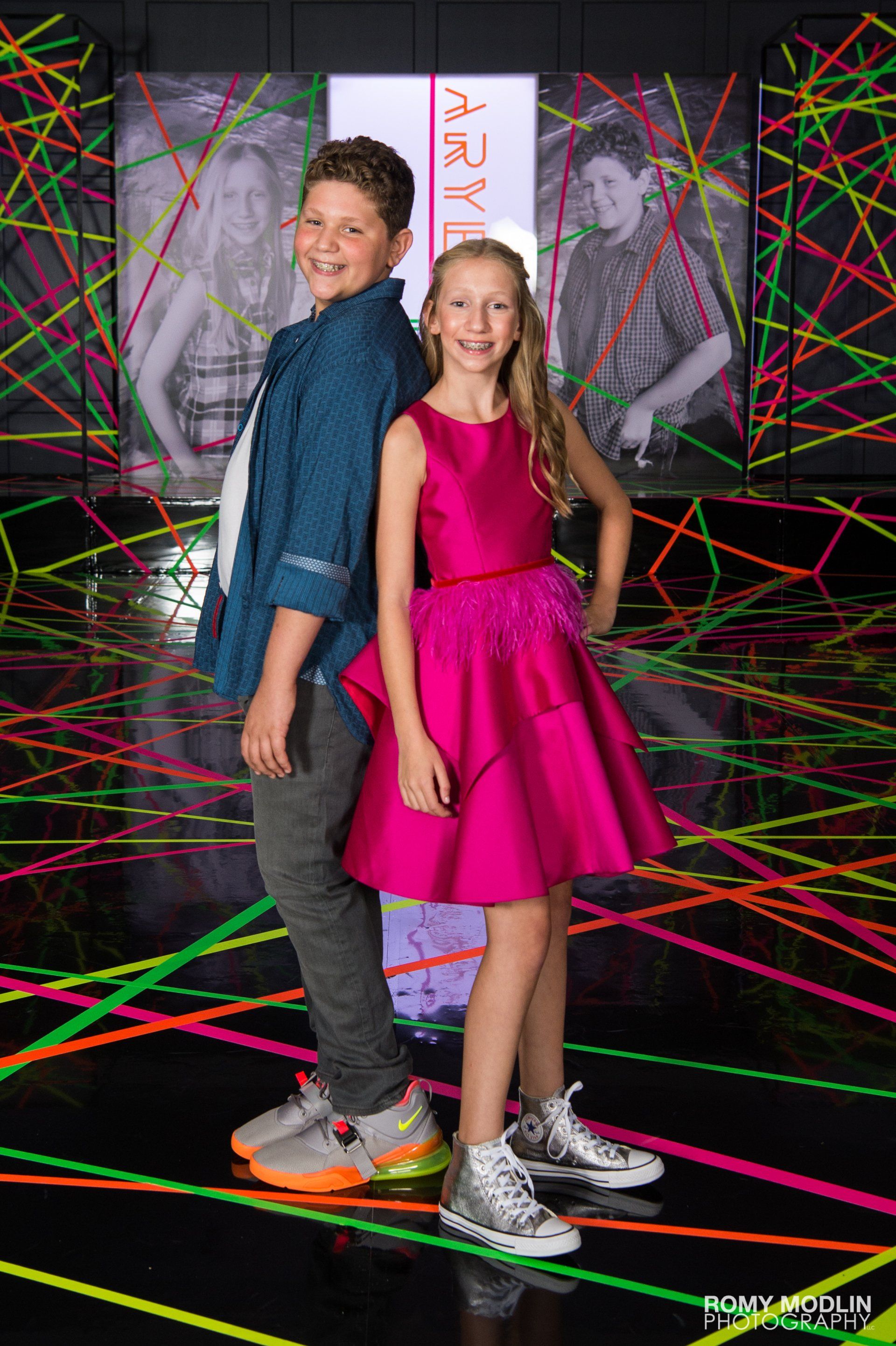 A boy and a girl are standing next to each other in front of a neon background.