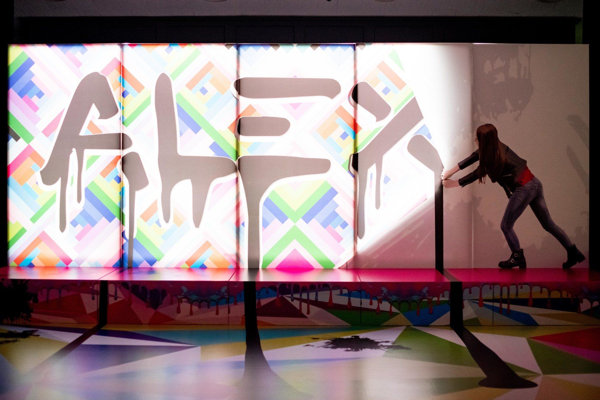 A woman is standing in front of a wall with the word alex painted on it.