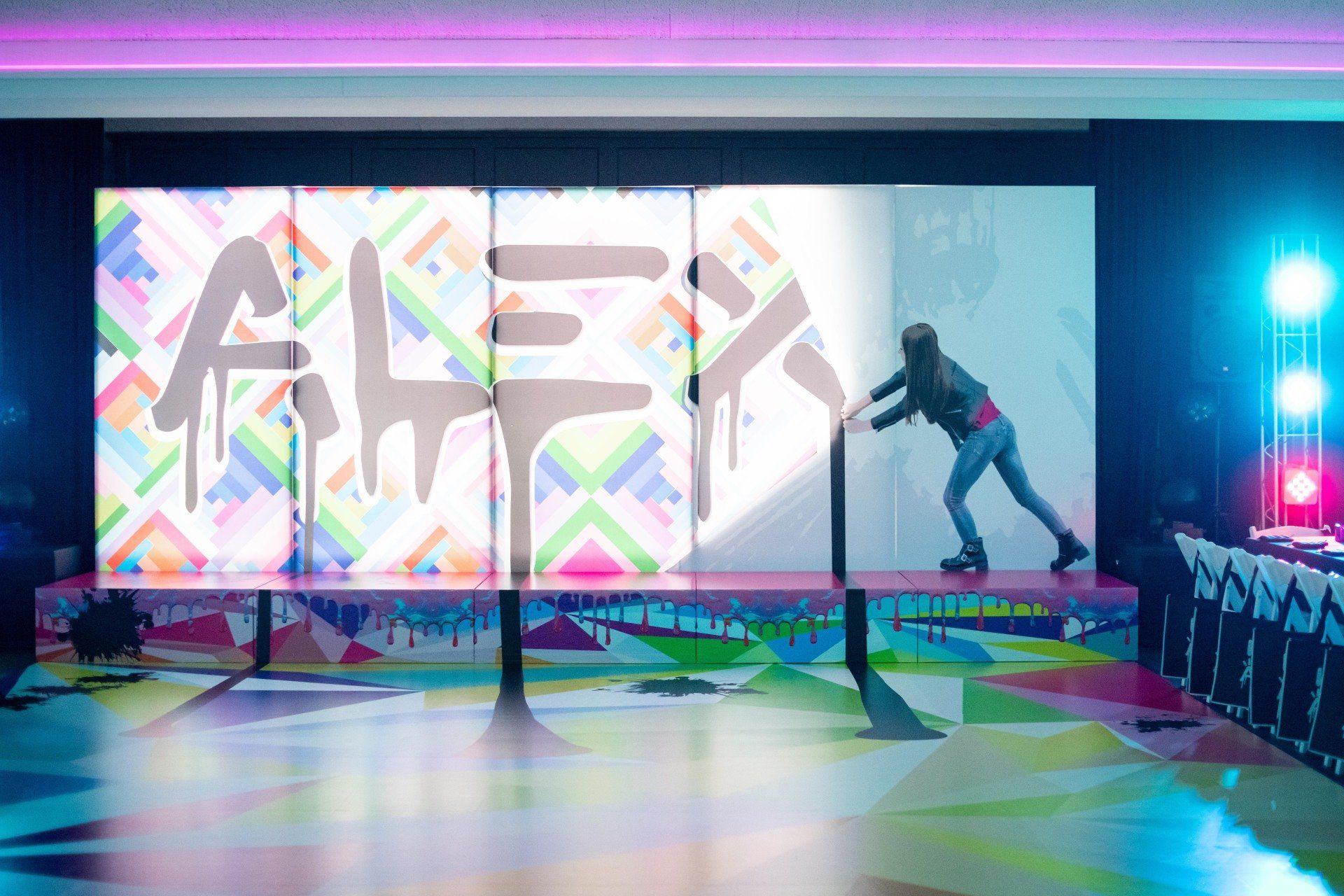 A woman is standing on a stage in front of a large screen that says alex.