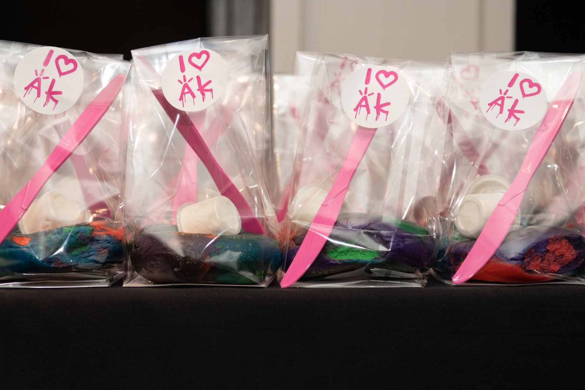 A row of plastic bags filled with candy and pink spoons.