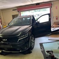 A black Kia SUV parked inside a workshop with its driver-side door open and the front end facing the camera.