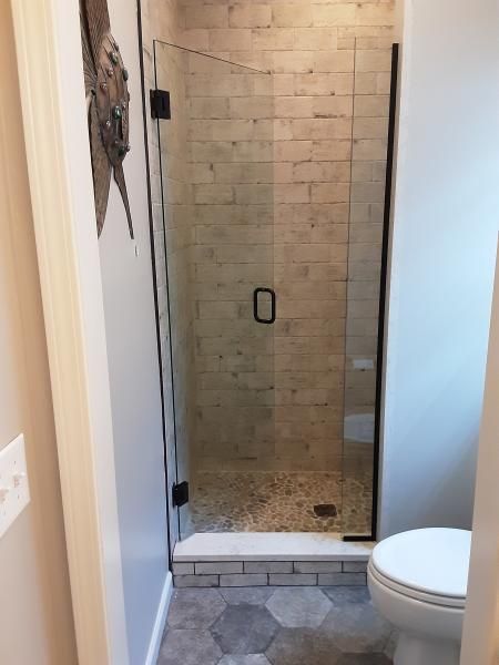 A small bathroom with a glass-enclosed walk-in shower featuring beige tiled walls and a pebble floor, next to a toilet.