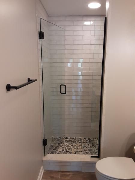 A walk-in shower with white subway tile walls, a pebbled floor, and a black-framed glass door, located next to a towel bar.