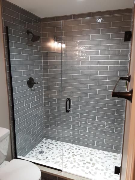 A glass-enclosed shower with gray rectangular subway tiles on the walls and a white pebble-style floor.