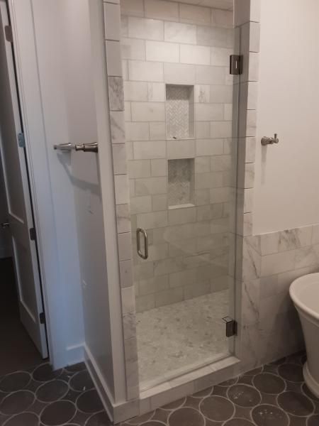A glass-door shower with light gray subway tile walls and built-in niches next to a freestanding tub in a modern bathroom.