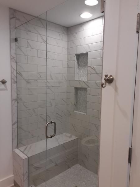 A glass-enclosed shower with white marble-patterned subway tiles, built-in wall niches, and a tiled bench seat.