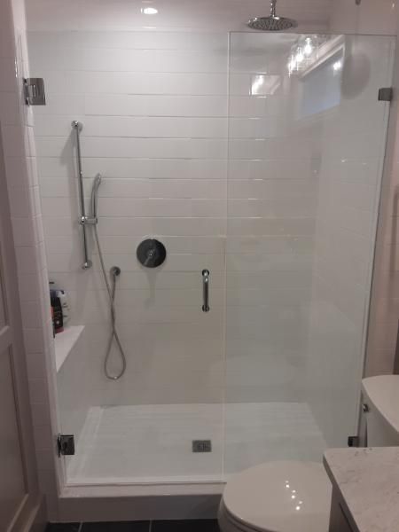 A modern walk-in shower with white subway tile walls, glass door, a rainfall showerhead, and a handheld spray.
