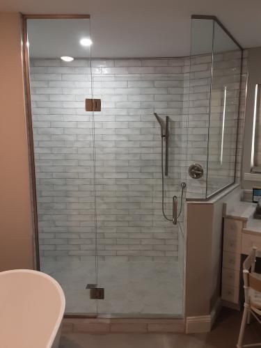 A glass-enclosed shower with white subway tile walls and a hand-held shower head, located in a modern bathroom.