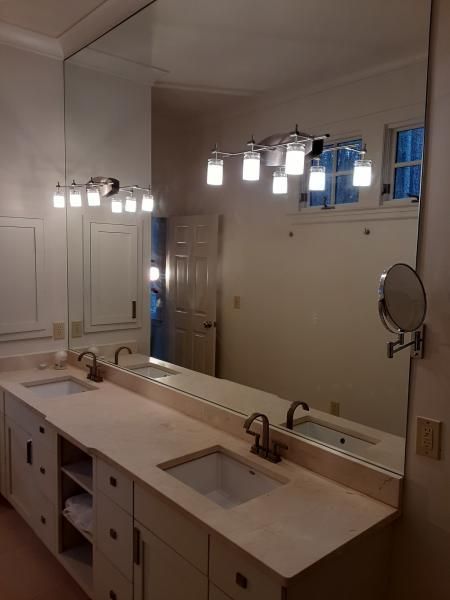 A bathroom vanity with dual sinks, a large mirror, two wall-mounted light fixtures, and open shelving between the drawers.