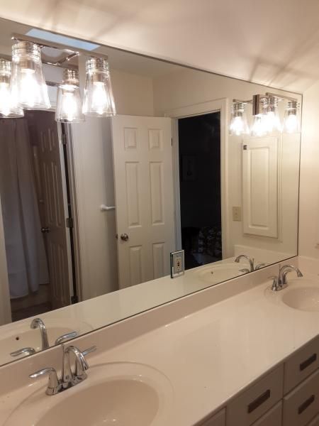 A bathroom vanity with a long wall-mounted mirror, two sinks with chrome faucets, and two modern light fixtures above.
