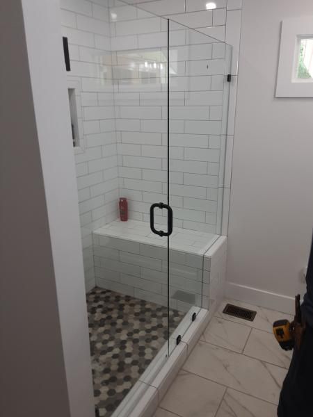 A tiled walk-in shower with a built-in bench, glass door with a black handle, and a pebble-tiled floor.
