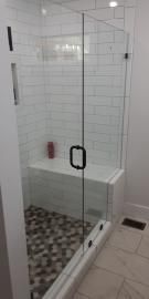 A modern walk-in shower with white subway tile walls, a pebble-tiled floor, a built-in bench, and a clear glass door.