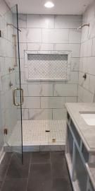 A walk-in shower with marble-look subway tile walls, a decorative recessed niche, a glass door, and dark tiled flooring.