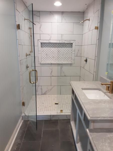 A modern bathroom featuring a glass-enclosed shower with white marble-look tiles, a mosaic niche, and dark gray floor tiles.