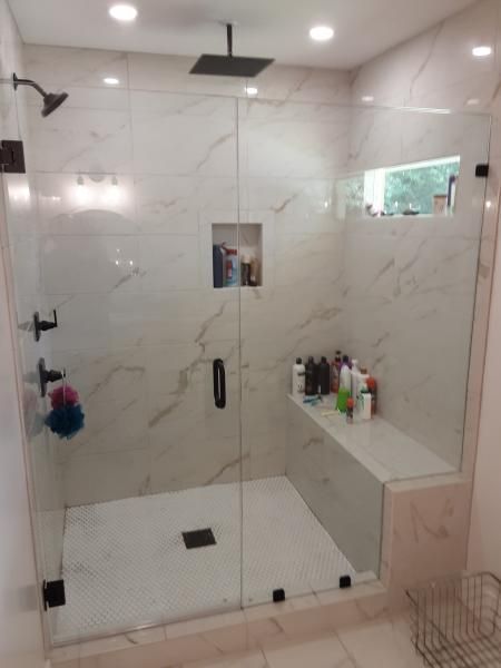 A modern walk-in shower with white marble-patterned tiles, a glass door, a bench, and matte black hardware fixtures.