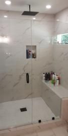 A modern walk-in shower with white marble tiles, a rain showerhead, a glass door, a built-in bench, and a wall niche.