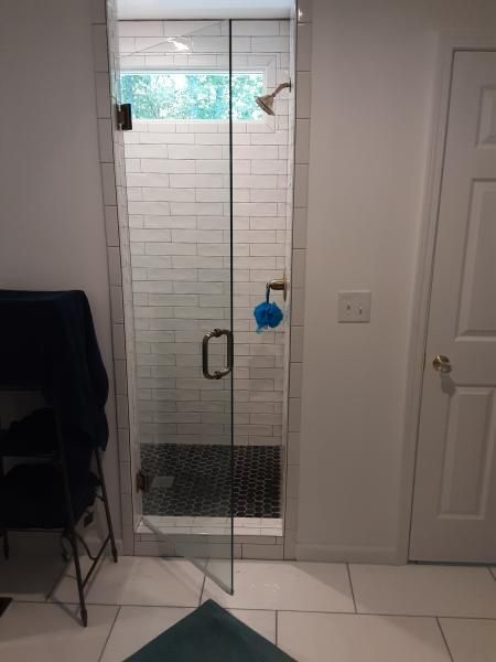 A walk-in shower with a glass door, light-colored subway tile walls, a dark hexagonal floor, and a blue bath sponge.