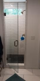 A modern glass-enclosed shower with white subway tile walls, a dark stone floor, and a hanging blue sponge.