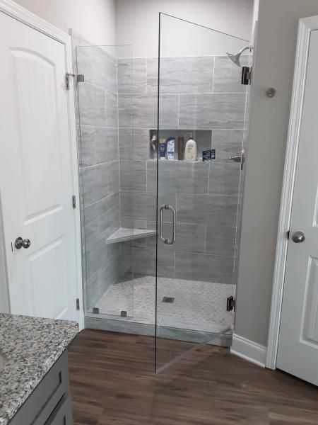 A modern walk-in shower with gray tile walls, a glass door, a built-in corner seat, and a recessed storage shelf.