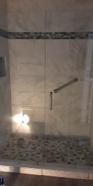 A glass-enclosed shower with tiled walls and a decorative mosaic border, featuring a metal grab bar and handle.