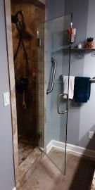 A glass shower door with a metal handle and grab bar, flanked by tiled walls and hanging towels in a bathroom.